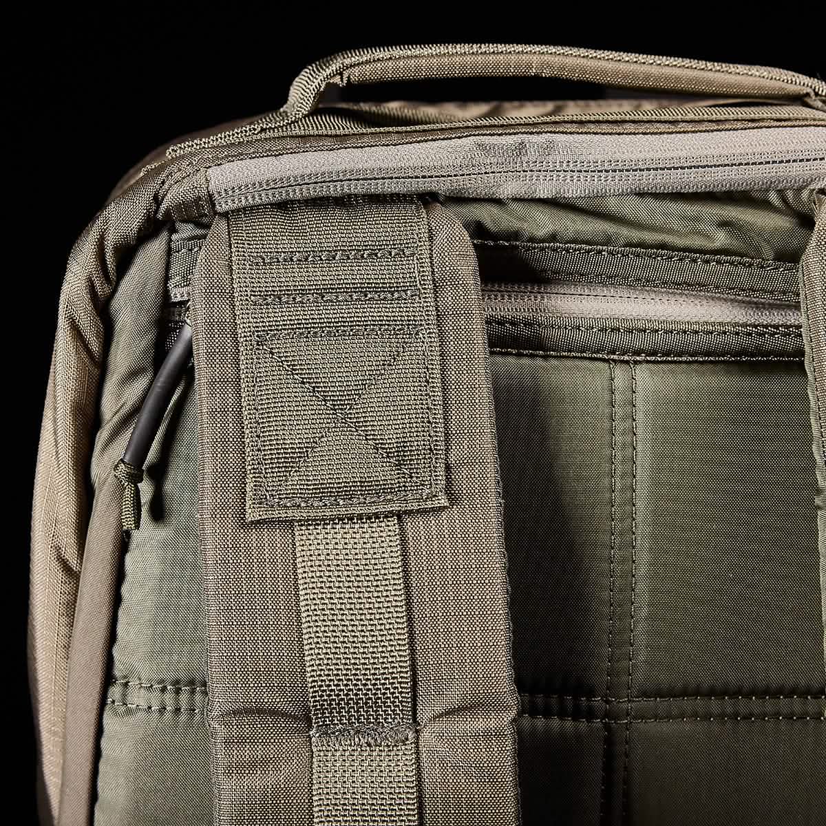 Close-up of a green GORUCK GR1 USA - Ripstop ROBIC® backpack displaying the top handle and back panel. The visible stitching showcases the durable, military-grade fabric and intricate stitched patterns. A zipper is partially visible on the upper section of this water-resistant backpack.