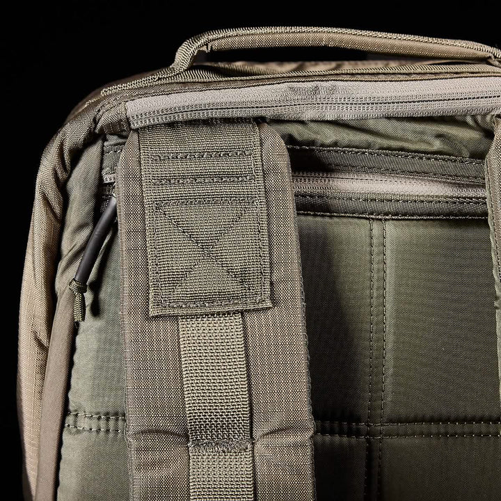 Close-up of a green GORUCK GR1 USA - Ripstop ROBIC® backpack displaying the top handle and back panel. The visible stitching showcases the durable, military-grade fabric and intricate stitched patterns. A zipper is partially visible on the upper section of this water-resistant backpack.