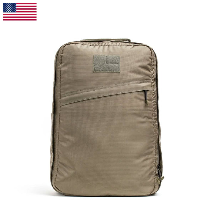 The GR1 USA - Ripstop ROBIC® by GORUCK is a lightweight khaki rucksack with a front zipper pocket and a patch area on top. It boasts a minimalist design made from water-resistant fabric for enhanced durability. An American flag adorns the top left corner of the image.