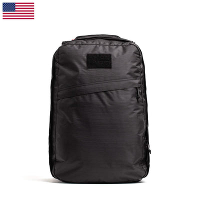 The GR1 USA - Dyneema by GORUCK is a black rucksack with a minimalist design, showcasing a zipper pocket on the front and a rectangular patch area. Constructed from durable Dyneema®, it features an American flag icon in the top left corner, reminiscent of the classic GR1 style.