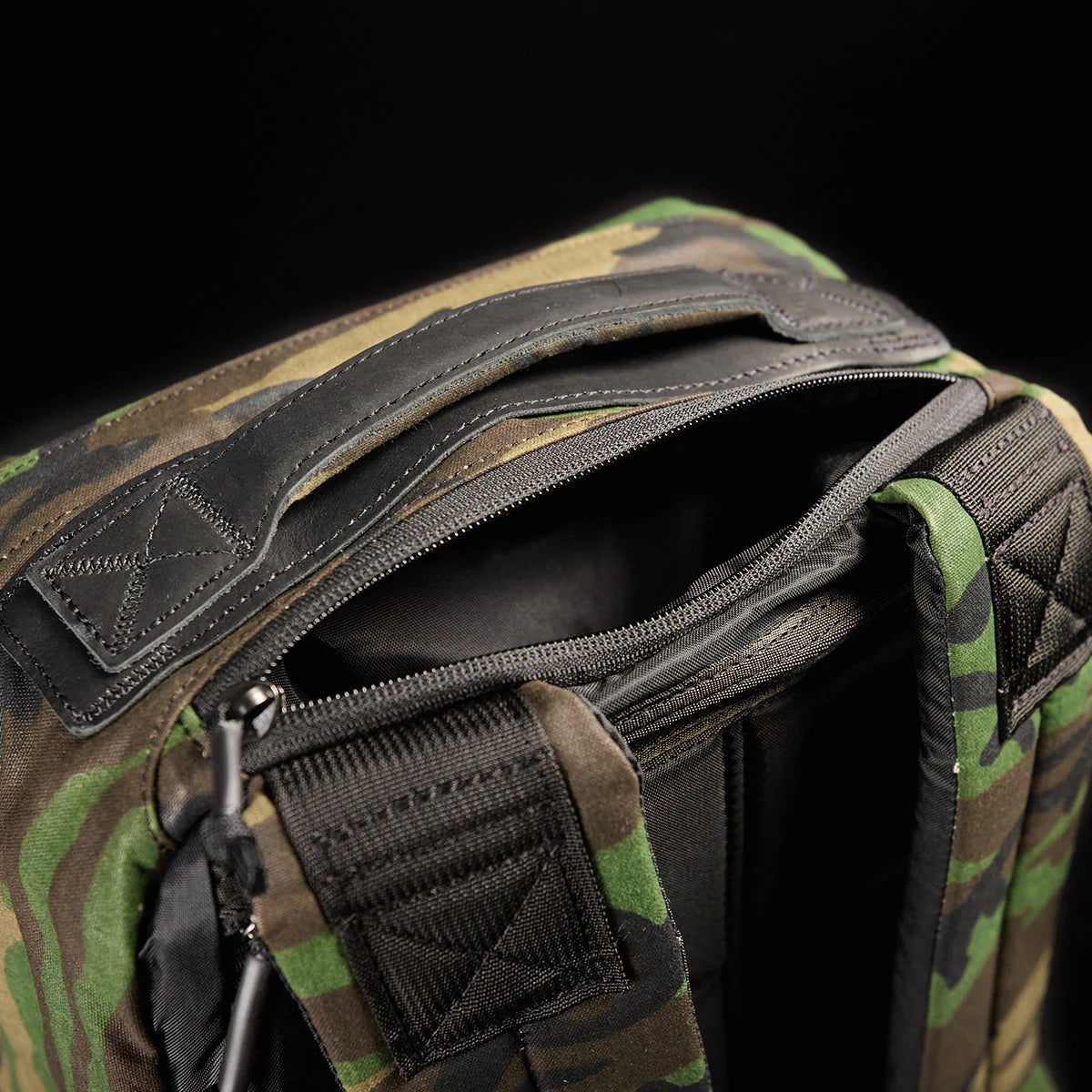 Close-up of the GR1 USA - Heritage Woodland Camo M81 backpack, featuring a zippered opening, padded straps, and reinforced handle—crafted in waxed canvas rucksack style.