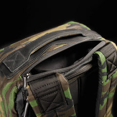 Close-up of the GR1 USA - Heritage Woodland Camo M81 backpack, featuring a zippered opening, padded straps, and reinforced handle—crafted in waxed canvas rucksack style.