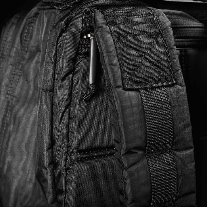 Close-up of the GR1 USA - Dyneema rucksack by GORUCK, showcasing its black color, durable stitching, and a secure zipper. The fabric's texture and padded straps reveal its rugged and sturdy design against a dark background that accentuates the intricate details.