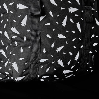 Close-up of the M23 - Cordura - Spearhead Shrapnel by GORUCK, showcasing a black fabric featuring a pattern of white abstract shapes resembling paper planes. This design is enhanced by intersecting black straps that add texture and highlight the use of durable materials in this geometric print.