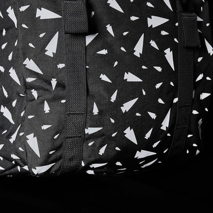 Close-up of the M23 - Cordura - Spearhead Shrapnel by GORUCK, showcasing a black fabric featuring a pattern of white abstract shapes resembling paper planes. This design is enhanced by intersecting black straps that add texture and highlight the use of durable materials in this geometric print.