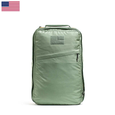 The GR1 USA - Ripstop ROBIC® by GORUCK is a lightweight green rucksack featuring a front zipper pocket and a small patch area on top. Its water-resistant design contrasts with the white background, highlighted by a small USA flag in the top left corner.