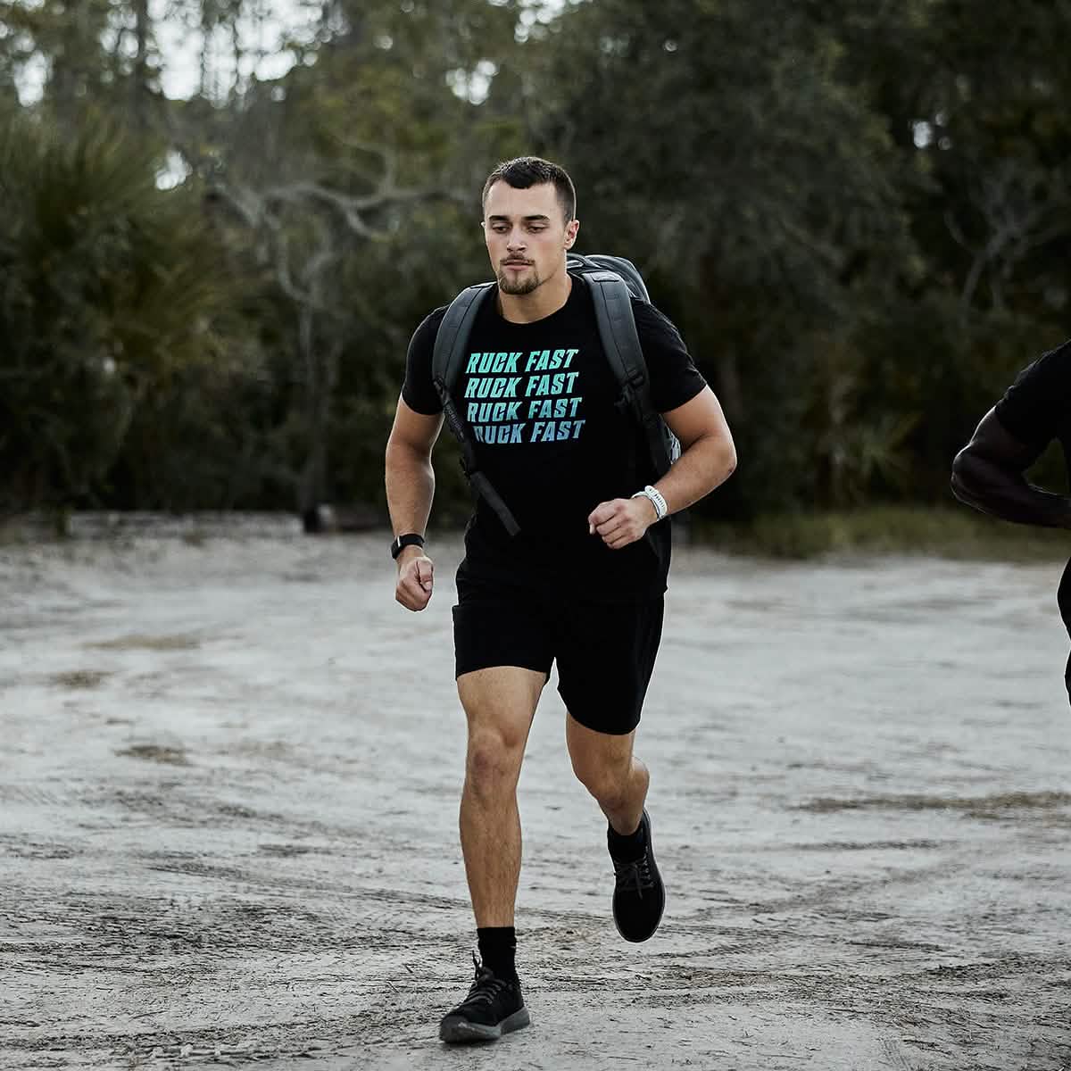 A person is rucking outdoors along a dirt path, clad in a 
