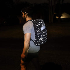 A man stands outside at night, facing away from the camera, wearing a headlamp and the Rucker 4.0 - Reflective Spearhead backpack.
