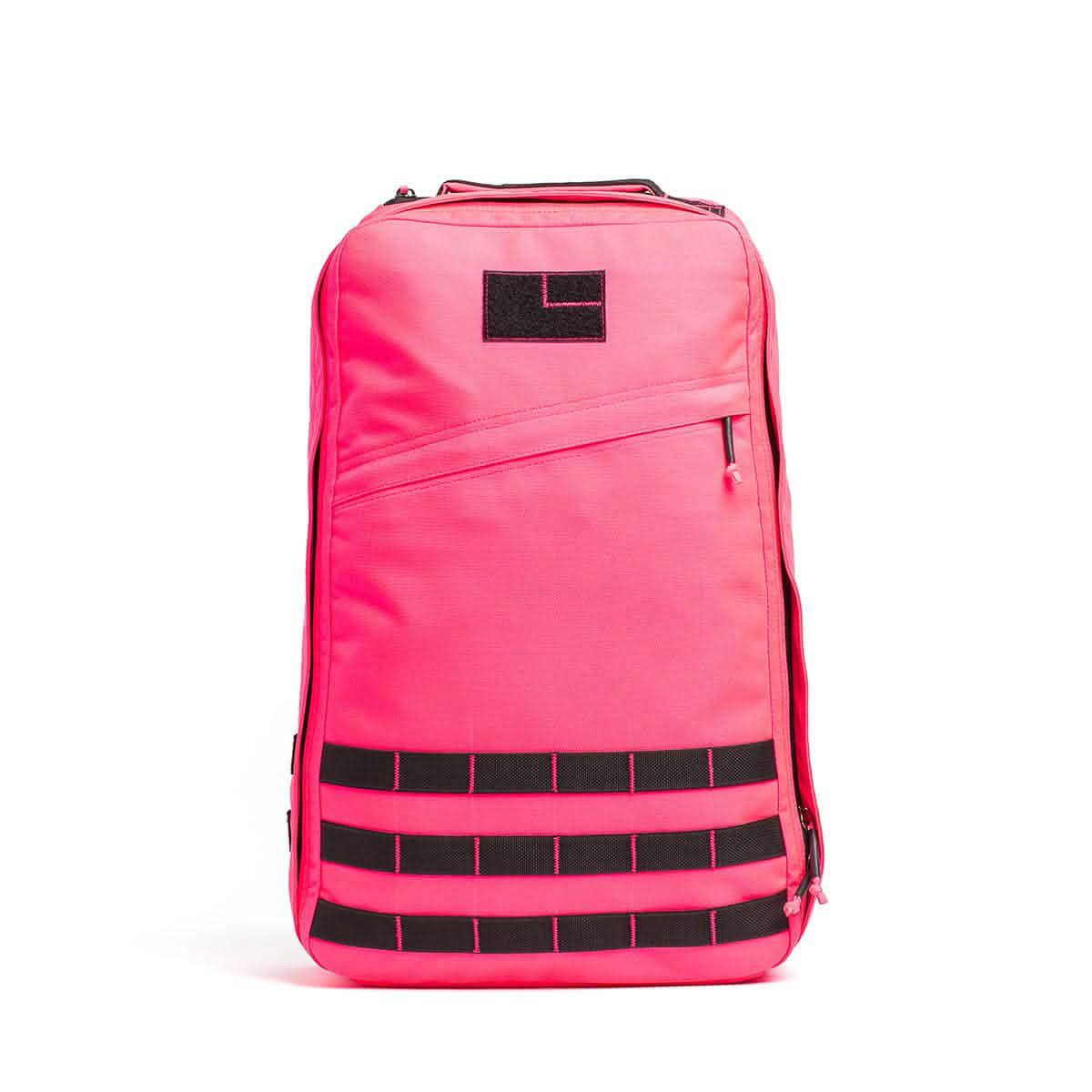 The GR1 USA - Cordura is a bright pink rucksack featuring a black patch and horizontal black straps on the lower front, inspired by Special Forces backpack design.