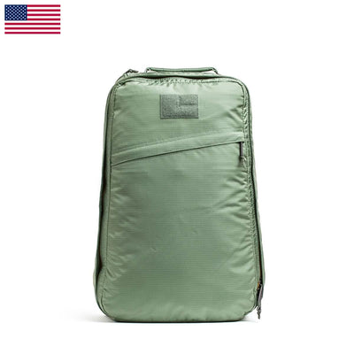 The GR1 USA - Ripstop ROBIC® backpack by GORUCK, a green rectangular design that is ultra lightweight and water resistant, includes a front zippered pocket. It is displayed against a plain white backdrop with an American flag in the top left corner, adding a patriotic element.