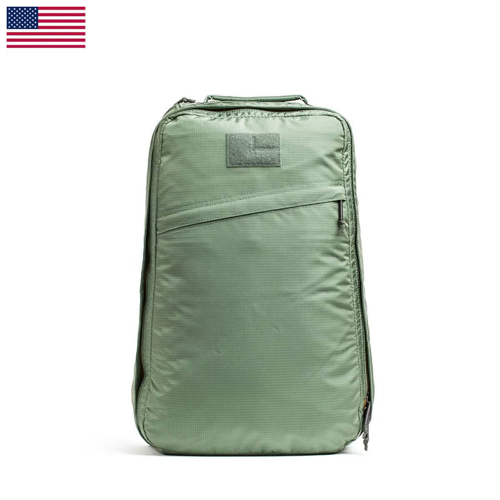 The GR1 USA - Ripstop ROBIC® backpack by GORUCK, a green rectangular design that is ultra lightweight and water resistant, includes a front zippered pocket. It is displayed against a plain white backdrop with an American flag in the top left corner, adding a patriotic element.