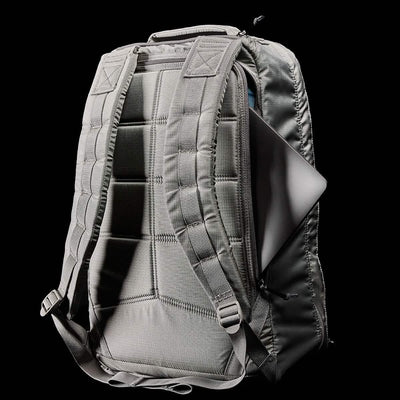 The GR1 USA - Ripstop ROBIC® by GORUCK is featured against a black background, showcasing its gray color and ultra-lightweight design. Padded shoulder straps enhance comfort as a laptop partially emerges from the back compartment, highlighting the backpack's metallic surface and water-resistant features.