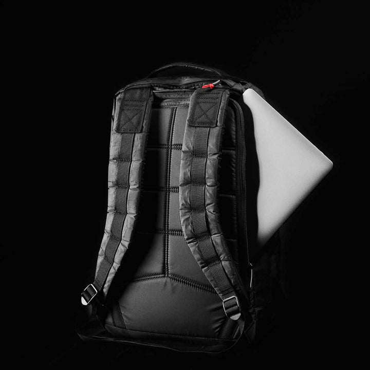 A black GR1 USA - Dyneema rucksack from GORUCK, featuring padded shoulder straps, is partially unzipped to reveal a silver laptop inside against a dark background. This sleek design ensures durability while maintaining style.