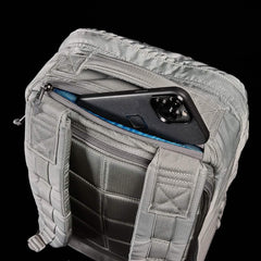 Close-up of gray tactical backpack back panel with padded straps and a smartphone partially tucked into a zippered pocket