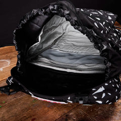 Open black rucksack with white geometric pattern showing padded interior compartments on wooden surface