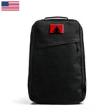 The GR1 USA x Carryology - GRXC2 Samurai is a black backpack made from Japanese cotton, featuring a red patch and a small U.S. flag in the upper left corner, shown upright.