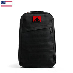The GR1 USA x Carryology - GRXC2 Samurai is a black backpack made from Japanese cotton, featuring a red patch and a small U.S. flag in the upper left corner, shown upright.