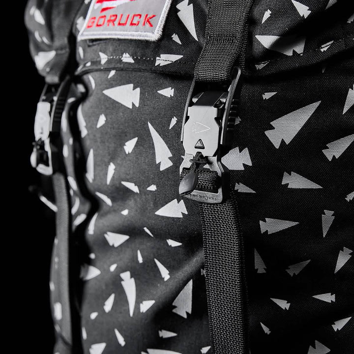Zoomed-in view of the GORUCK M23 - Cordura - Spearhead Shrapnel, a contemporary rucksack adorned with white arrow patterns, constructed from durable materials, and equipped with straps and buckles.