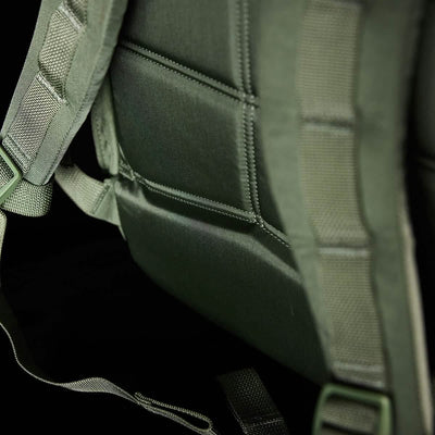 The close-up of the olive green GORUCK KR1 kids rucksack emphasizes its durable fabric and stitching, complemented by a padded back and adjustable straps, perfectly suited for carrying school supplies comfortably against a dark background.