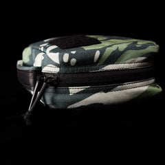 The GR1 Field Pocket x Gear Patrol by GORUCK, a small zippered pouch displaying a Variegated Elephant Ear Camo pattern in green with white spots and black accents, sits against a dark background. The partially unzipped design reveals its sleek black inner lining, perfect for any Gear Patrol adventure.