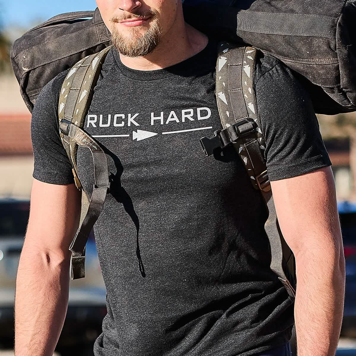 A fitness enthusiast walks through the sunny outdoors with a large backpack, wearing his 