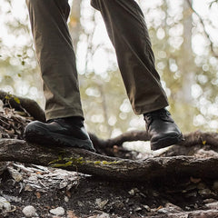 Close-up of black tactical boots on rugged forest ground with tree roots and fallen leaves