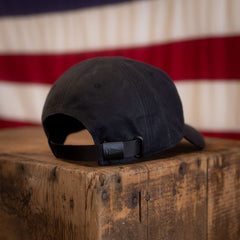 A Tac Hat - Heritage rests atop a wooden box with a softly blurred American flag in the background.