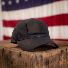 A Tac Hat – Heritage rests on a wooden surface, with a blurred American flag in the background.