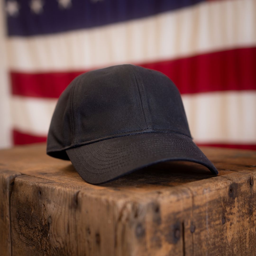 Tac Hat - Heritage resting on a rustic wooden table with a blurred American flag in the background.