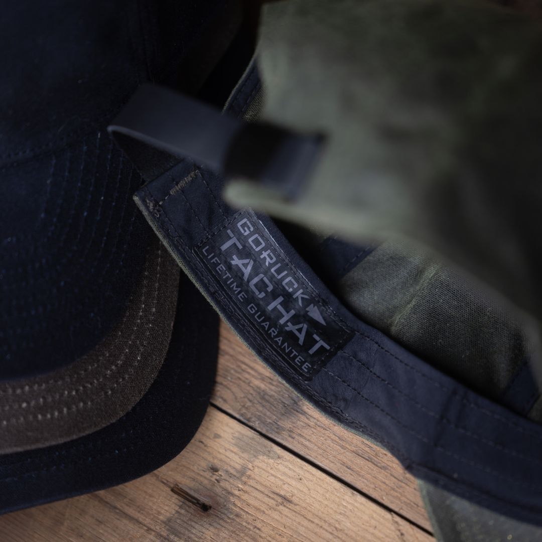 Close-up of a Tac Hat - Heritage with a visible label reading “Lifetime Guarantee” on a wooden surface.