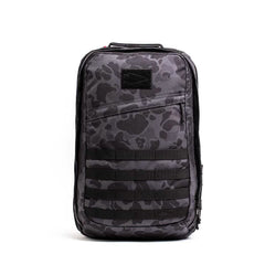 A GORUCK GR2 backpack in gray camouflage with black straps and multiple compartments stands upright against a plain white background. The design, inspired by Special Forces rucks, features horizontal webbing on the front.