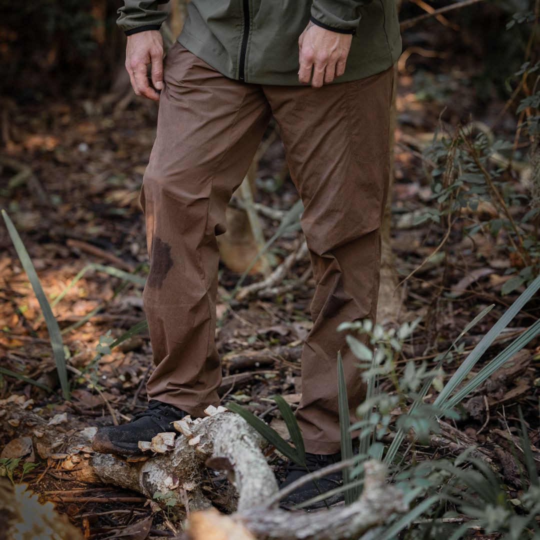 A person wearing an olive jacket and abrasion-resistant, fast-drying trousers standing in a wooded area.