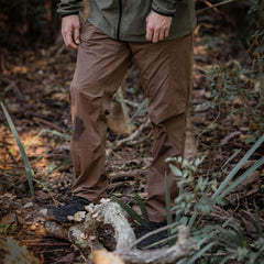 A person wearing an olive jacket and abrasion-resistant, fast-drying trousers standing in a wooded area.