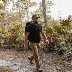 A man with the Rucker - Long Range rucksack hikes a lush, forested trail, embracing the thrill of distance rucking.