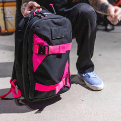 GORUCK black rucksack with bright pink straps, held by a person kneeling on concrete