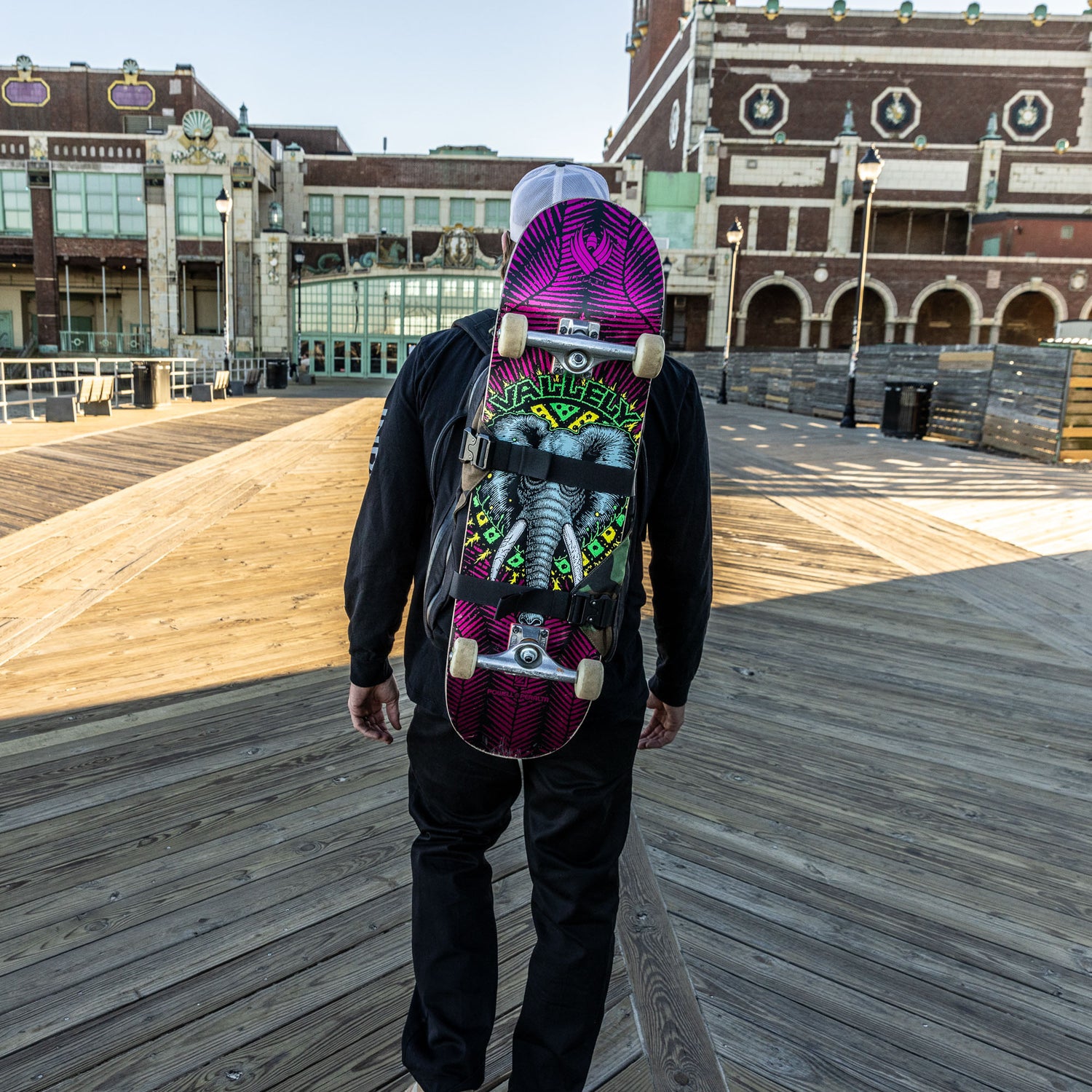 A person carrying the Skate Ruck walks along a wooden boardwalk past historic, ornate buildings.
