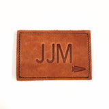 Patch - Custom Leather Monogram: brown leather patch embossed with custom initials "JJM" and an arrow symbol—perfect for adding a unique, personalized touch.