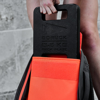 A hand places a Ruck Bundle into a backpack with a bright orange pocket.