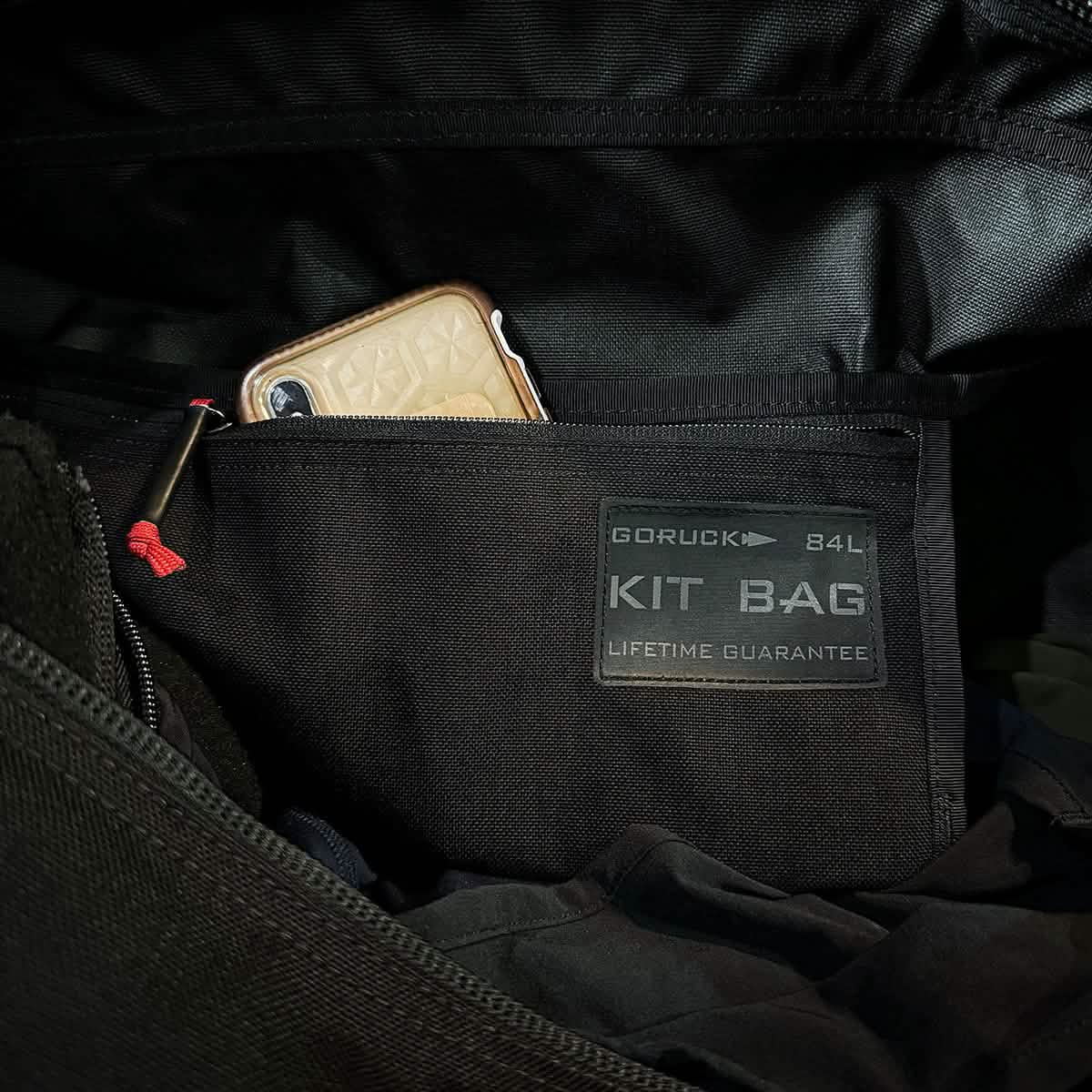 A smartphone fits snugly in the pocket of a black GORUCK Kit Bag (Includes Shoulder Strap) labeled 