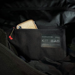 A smartphone fits snugly in the pocket of a black GORUCK Kit Bag (Includes Shoulder Strap) labeled "84L" and "Lifetime Guarantee," embodying the rugged resilience favored by Special Forces.