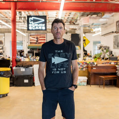 A man is standing in a workshop, wearing the “Easy Life Is Not For Us” black shirt.