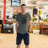 A man stands in an office wearing the “In GOD We Trust” t-shirt and shorts, looking at the camera.
