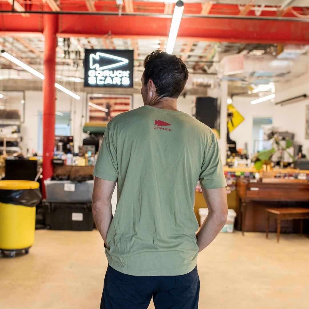 Wearing an AmeRUCKa green t-shirt, a person stands in a spacious, well-lit workshop with their back to the camera.