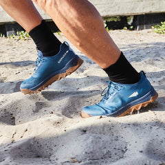 Close-up of person wearing blue GORUCK trail running shoes with black socks on sandy terrain