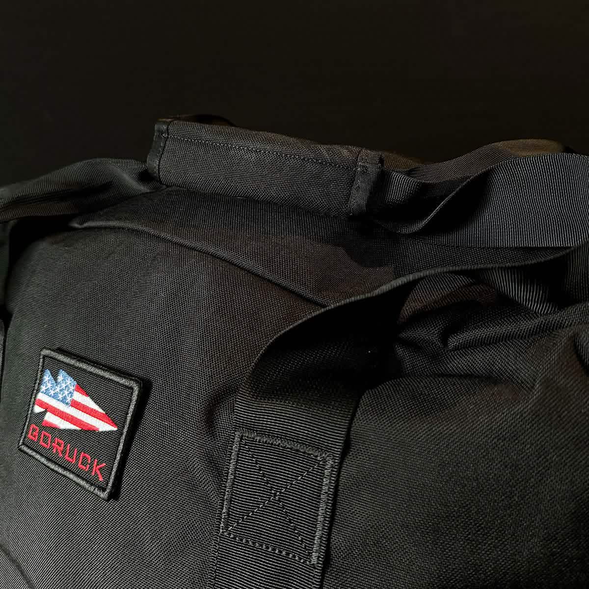 A close-up of a black Kit Bag (Includes Shoulder Strap) featuring a stylized American flag patch and the word 