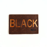 The Patch - Custom Leather Monogram is a brown leather patch, personalized with "BLACK" embossed in gold and accented with a small arrow symbol in the corner.
