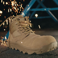 The MACV-2 Safety Boot - Mid Top by GORUCK stands on a hard surface, with glowing sparks in the background, evoking an industrial or construction setting.