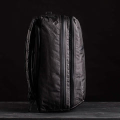 The GR2 USA x Carryology - Ultra Black backpack, made from Challenge Sailcloth UHMWPE, stands upright with visible zippers against a dark background.