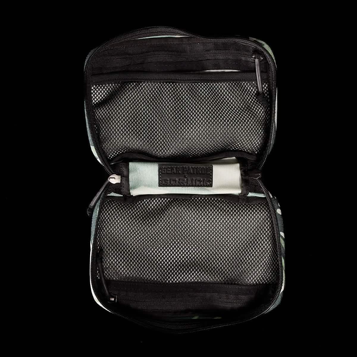 A GR1 Field Pocket x Gear Patrol by GORUCK with a Variegated Elephant Ear Camo pattern features two zippered mesh compartments against a black background. Inside, the center displays a Bear & Path label, reminiscent of the gear recommended for outdoor enthusiasts on Gear Patrol.