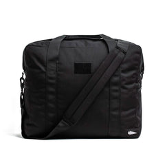 A stylish, black Kit Bag from GORUCK, inspired by an Aviator’s Kit Bag, equipped with dual handles and an adjustable shoulder strap. It boasts a minimalist design with a subtle logo placed near the bottom corner against a plain white backdrop.